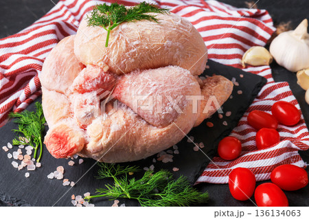 Whole frozen chicken with frost on black slate board with dill, garlic and tomatoes. Raw poultry meat ready for cooking on striped towel background. High quality photo Whole frozen chicken with frost on black slate board with dill, garlic and tomatoes. Raw poultry meat ready for cooking on striped towel background. High quality photo 136134063