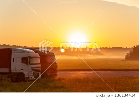 Sun rising over two parked trucks by the roadside, with mist in the field. Sun rising over two parked trucks by the roadside, with mist in the field. 136134414