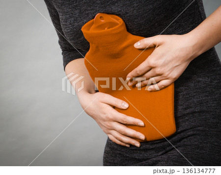 Girl having stomach ache, holding hot water bottle 136134777