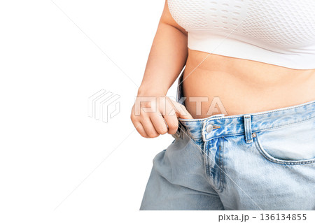Woman showing weight loss results by pulling oversized jeans away from waist. Slimmed female body in loose pants after successful diet isolated on white background. High quality photo 136134855