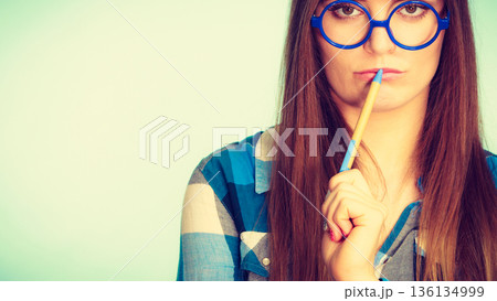 Nerdy thinking woman in glasses holding pen Nerdy thinking woman in glasses holding pen 136134999
