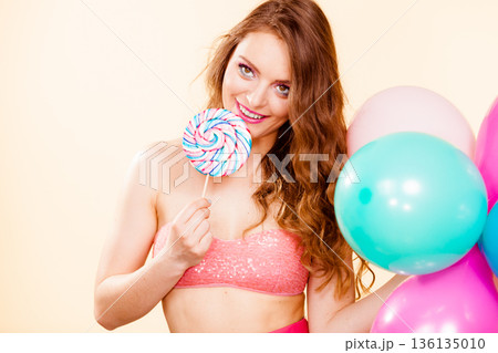 Woman holds lollipop candy and balloons 136135010