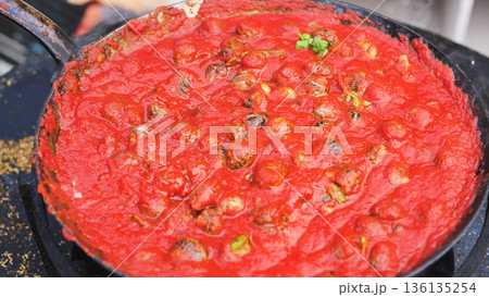 The chef pours oil over snails in tomato sauce. 136135254