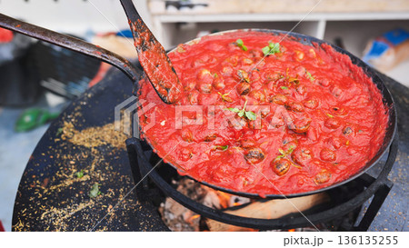 Snails cooking in tomato sauce over open fire 136135255