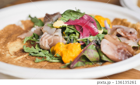 Savory crepe with fresh greens, ceviche, pickled onions, and a colorful sauce 136135261