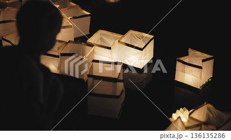 Paper lanterns gently floating on dark water at night, creating a peaceful atmosphere. 136135286