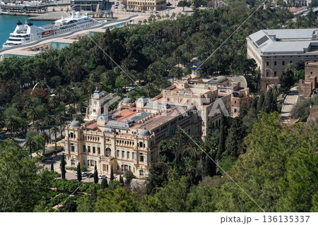 View of Malaga city hall Ayuntamiento de Malaga with clock tower, historic architecture and palm trees in park, cruise ship at harbor, Spain 136135337