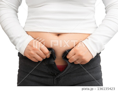 Close up of woman struggling to zip up tight jeans due to weight gain. Overweight female belly isolated on white background Close up of woman struggling to zip up tight jeans due to weight gain. Overweight female belly isolated on white background 136135423