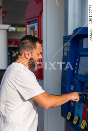 A man is standing in front of a gas pump, putting money into the machine A man is standing in front of a gas pump, putting money into the machine 136135777