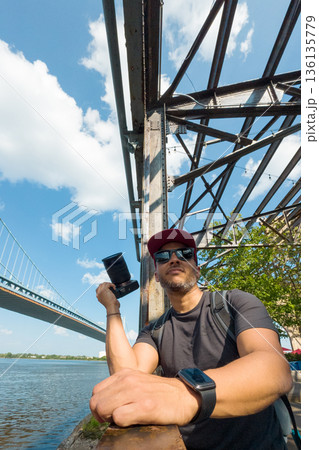 A man is sitting on Benjamin Franklin bridge holding a camera 136135779