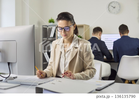 Accountant woman doing finance analysis at computer while colleagues meet in office Accountant woman doing finance analysis at computer while colleagues meet in office 136135790