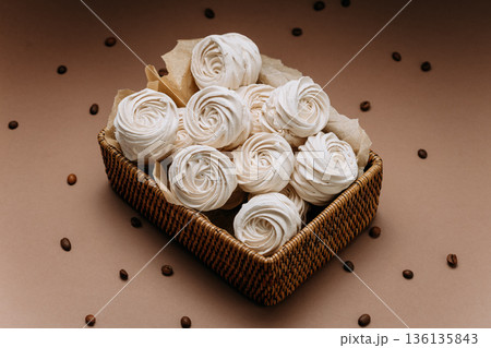 White meringue rosettes in wicker basket with coffee beans, beige copy space White meringue rosettes in wicker basket with coffee beans, beige copy space 136135843