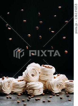 Flying coffee beans over vanilla zephyr swirls on dark background, copy space Flying coffee beans over vanilla zephyr swirls on dark background, copy space 136135853