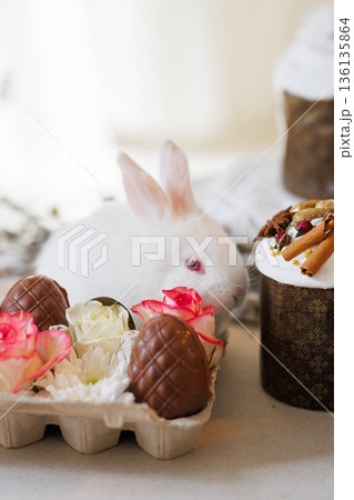 White bunny with chocolate eggs and roses in carton, Easter still life, soft bokeh White bunny with chocolate eggs and roses in carton, Easter still life, soft bokeh 136135864