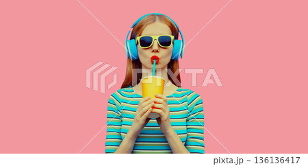 portrait of stylish young woman listening to music with headphones drinking fresh juice portrait of stylish young woman listening to music with headphones drinking fresh juice 136136417