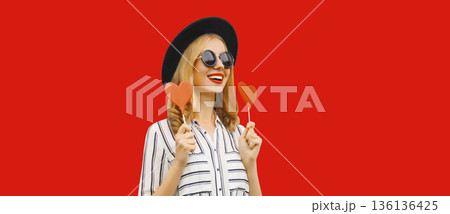 happy cheerful young woman with sweet red heart shaped lollipop on stick 136136425