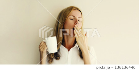 Sleepy lazy woman yawns waking up after sleeping holds cup of coffee in morning on white background Sleepy lazy woman yawns waking up after sleeping holds cup of coffee in morning on white background 136136440