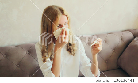 Sick young woman sneezing blow nose using tissue and measuring checking body temperature at home Sick young woman sneezing blow nose using tissue and measuring checking body temperature at home 136136441