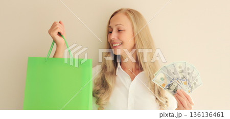 Happy smiling middle aged woman with shopping bags holding cash money in dollar bills in hands 136136461