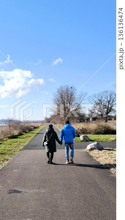A loving couple walks hand in hand along an asphalt path in a park on a sunny day A loving couple walks hand in hand along an asphalt path in a park on a sunny day 136136474