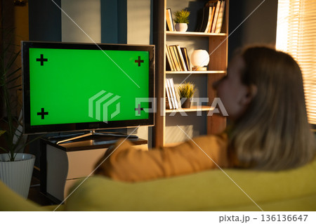 Woman relaxing on a sofa in a modern living room, watching the green screen tv, representing concepts of home entertainment, streaming, and relaxing in the evening Woman relaxing on a sofa in a modern living room, watching the green screen tv, representing concepts of home entertainment, streaming, and relaxing in the evening 136136647