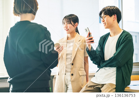 スマホを持ちながら談笑をする若い男女 スマホを持ちながら談笑をする若い男女 136136753