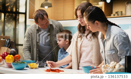 Parents teaching their children to make delicious homemade pizza, pre-teen girl and little boy being involved and learning to cook together. Family moment during weekend activity. 136137533