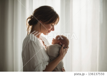 窓辺の自然光で新生児を抱く母親の横顔 136137550