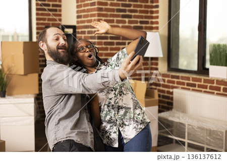 Caucasian man holds cellphone while attending online call with African American girlfriend, sharing updates with family. Happy multiethnic couple warmly greeting loved ones during video conference. 136137612