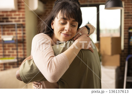 Warm embrace in brick wall apartment as young multiethnic couple celebrate newly purchased property. Caucasian woman smiling in comfort, hugging boyfriend in living room of new home. Warm embrace in brick wall apartment as young multiethnic couple celebrate newly purchased property. Caucasian woman smiling in comfort, hugging boyfriend in living room of new home. 136137613