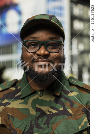 Portrait of african american military soldier walks through downtown center, camouflage gear and focused expression representing courage and commitment. Standing in uniform among buildings. 136137622