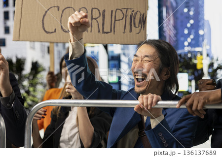 Asian man annoyed screaming at political protest with large protesters crowd, taking action against corrupt government, posters with messages like stop corruption and equal rights. 136137689