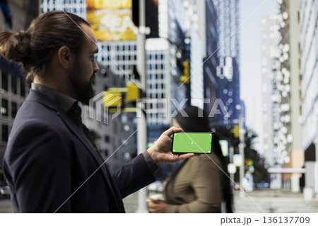 Horizontal green screen on phone held by male professional near urban motion of diverse pedestrians crowd on downtown street captures city life, diversity and the daily realistic routine. 136137709