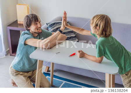 Father and his son assembling a table together in the living room at home. Meaningful family moment showing teamwork, learning and support. Fatherhood, home improvement and bonding through shared 136138204