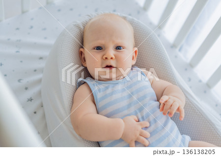 Baby lying peacefully in a cozy cocoon nest inside a crib, feeling safe and calm at home. Soft light and warm atmosphere highlight comfort and care. Infant sleep, safety and gentle parenting concept 136138205