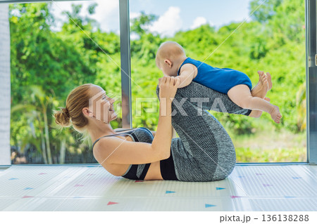 Mother doing fitness exercises while holding her baby at home, combining workout and childcare. Real lifestyle moment showing balance, strength and love. Postpartum fitness, healthy motherhood and 136138288