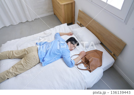 私服でベッドで寝る疲労した男性 136139443