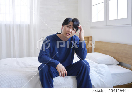 ベッドに座る20代男性　頭痛 136139444