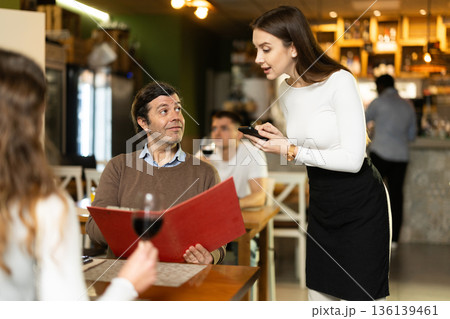 Girl waiter communicates with male customer, serve couple in restaurant Girl waiter communicates with male customer, serve couple in restaurant 136139461