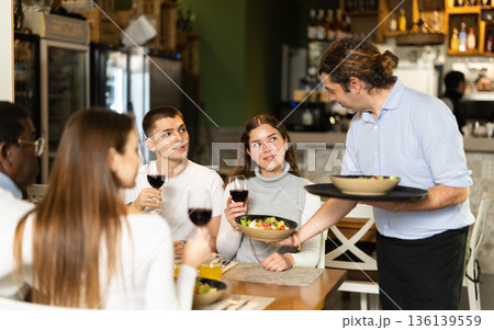 Man waiter serves cafe establishments couple visitor, puts food on table. 136139559