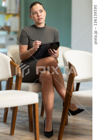 Young girl student dressed in business dress sitting and listening lecture, taking notes on tablet in lecture hall Young girl student dressed in business dress sitting and listening lecture, taking notes on tablet in lecture hall 136139595
