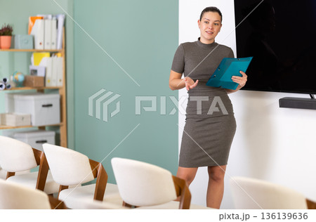 Female coach with folder with papers standing near blackboard in classroom Female coach with folder with papers standing near blackboard in classroom 136139636