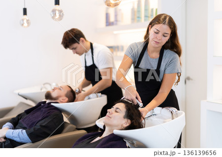 Young woman stylist washes female clients hair, prepares it for cutting and styling 136139656