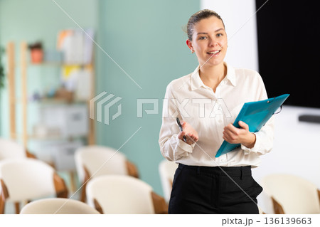 Girl office employee with folder greets and invite visitors Girl office employee with folder greets and invite visitors 136139663
