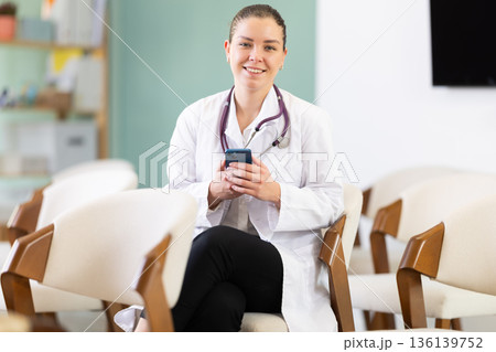Attentive positive young girl medical student sitting and listening lecture, taking photo or QR with mobil in lecture hall 136139752