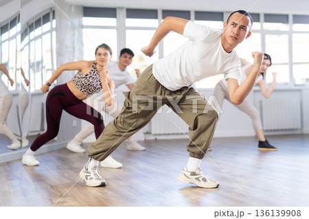 Positive young men and girls dancing modern street dance together during their group training at dance hall Positive young men and girls dancing modern street dance together during their group training at dance hall 136139908