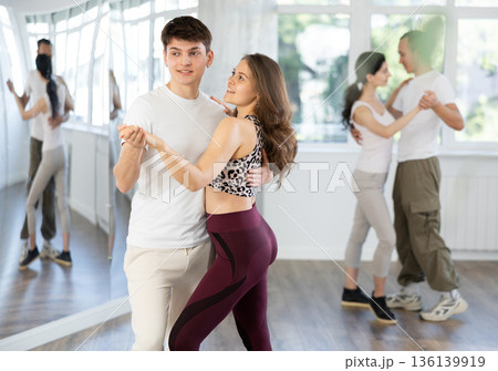 Girl paired up with young man, they train to perform slow waltz dance, rehearse performance. Girl paired up with young man, they train to perform slow waltz dance, rehearse performance. 136139919