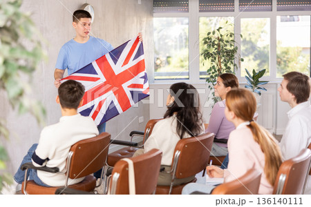 Young teacher holding flag of Great Britain in front of group of students Young teacher holding flag of Great Britain in front of group of students 136140111
