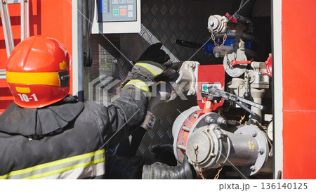 Firefighter connecting a water hose to a pump on a fire engine during an emergency 136140125