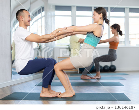Women and men performing paired yoga exercises during group training at gym. Fitness and pair Hatha yoga concept. Women and men performing paired yoga exercises during group training at gym. Fitness and pair Hatha yoga concept. 136140187